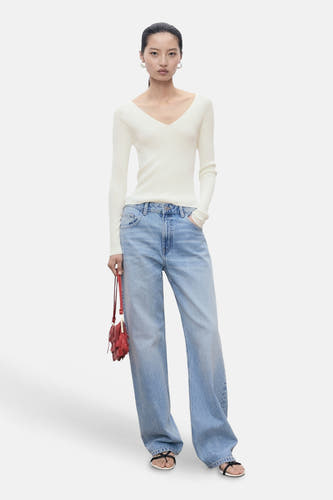 Witte trui met ronde hals van MANGO, gecombineerd met wijde jeans en een rode tas met franjes.
