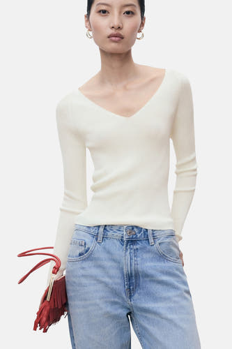 Witte trui met ronde hals van MANGO, gedragen met een blauwe spijkerbroek en een rode tas met franjes.

