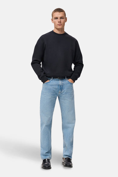 Pull-over bleu de MANGO, porté avec des jeans légers et des chaussures en cuir noires, les mains dans les poches.