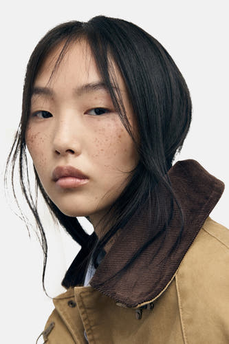 Beige korte jas van MANGO, met bruine kraag en losse haren.