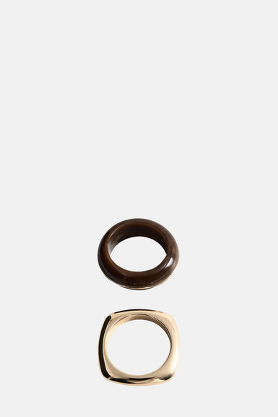 Gouden armband van MANGO, met een afgerond vierkant ontwerp, onder een bruine armband.
