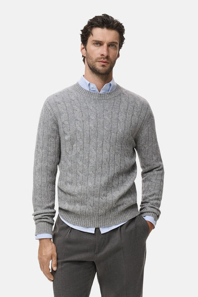 Sweat-shirt gris à col rond de MANGO, avec un motif côtelé et porté sur une chemise bleu clair, associé à un pantalon gris.