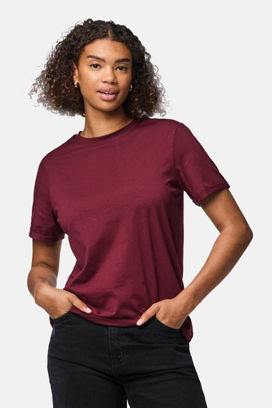 Bordeaux T-shirt met korte mouwen van PIECES®, gedragen met zwarte jeans en gouden oorbellen.
