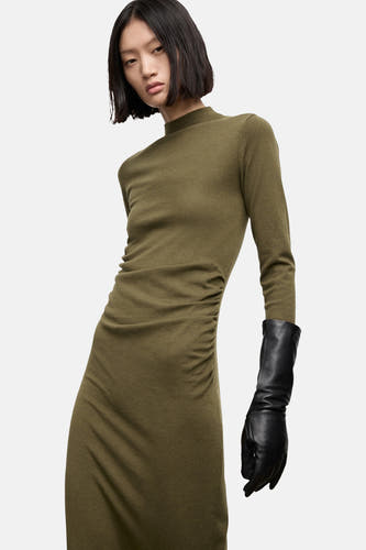Khaki jurk met lange mouwen van MANGO, met plooien aan de zijkant en een zwarte leren handschoen.
