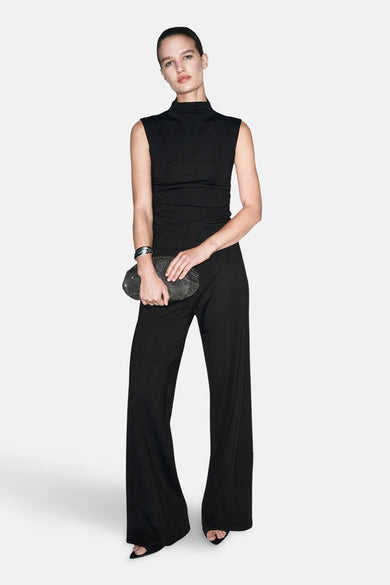 Zwarte broek van MANGO, met wijde pijpen en gecombineerd met een clutch en een zilveren armband.
