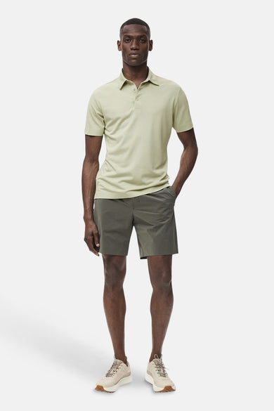 Polo vert de manches courtes de MANGO, avec un design simple, associé à des shorts olive et des chaussures beige.