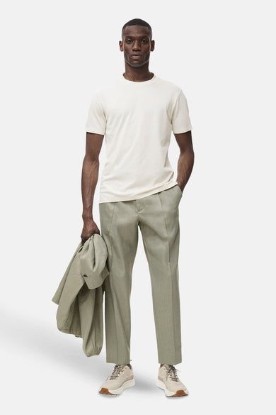 T-shirt écru à manches courtes de MANGO, porté avec un pantalon vert et des baskets, avec un manteau sur le bras.