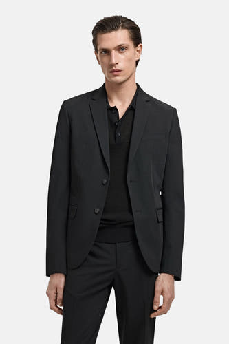Zwarte blazer van MANGO, gedragen met een zwart poloshirt en pantalon.
