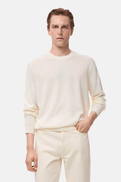 T-shirt écru avec col rond de MANGO, associé à des jeans crème, avec une main dans la poche.
