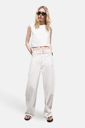 Ecru mouwloze blouse van MANGO, gedragen met een witte broek met riem en zwarte slippers.