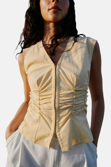 Gele mouwloze blouse van MANGO, met gerimpelde details en een zilveren ketting.
