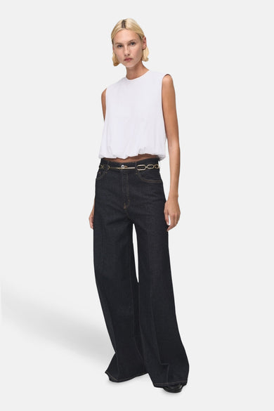 T-shirt sans manches blanc de MANGO, avec un détail plissé et associé à des jeans larges foncés et une ceinture en chaîne d'or.