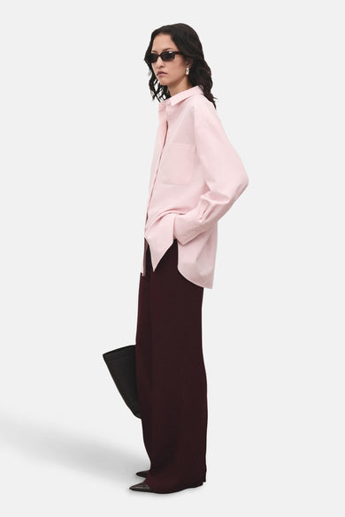 Chemise rose à manches longues de MANGO, portée avec un pantalon large et une poche main noire.