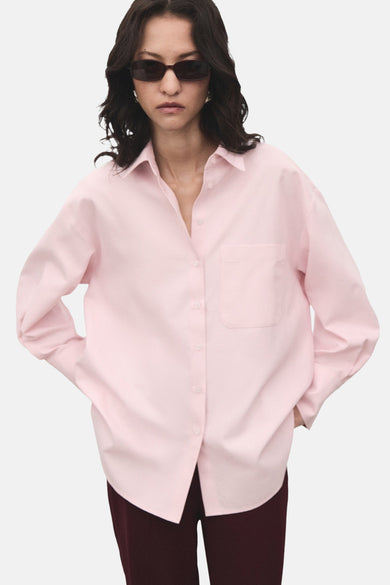 Chemise rose à manches longues de MANGO, avec une poche poitrine et portéeée un pantalon sombre et un chapeau de soleil.