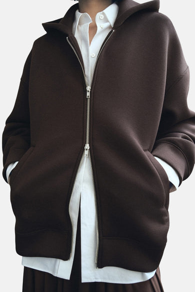 Bruine sweater gilet van MANGO, met zilverkleurige rits en steekzakken, over een wit overhemd.
