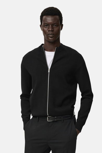 Gilet noir de MANGO, porté sur un T-shirt blanc et associé à une jupe noire avec ce ce.