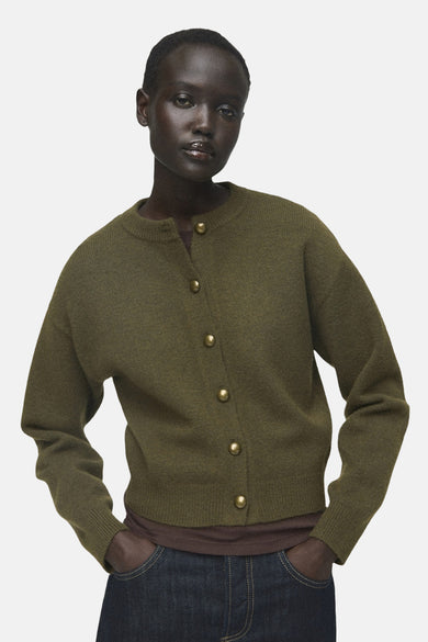 Khaki gilet van MANGO, gedragen over een bruin shirt en donkerblauwe jeans met de handen in de zakken.
