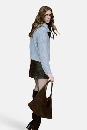 Grijs gilet van MANGO, gedragen over een leren rok, met een bruine tas en hoge laarzen.
