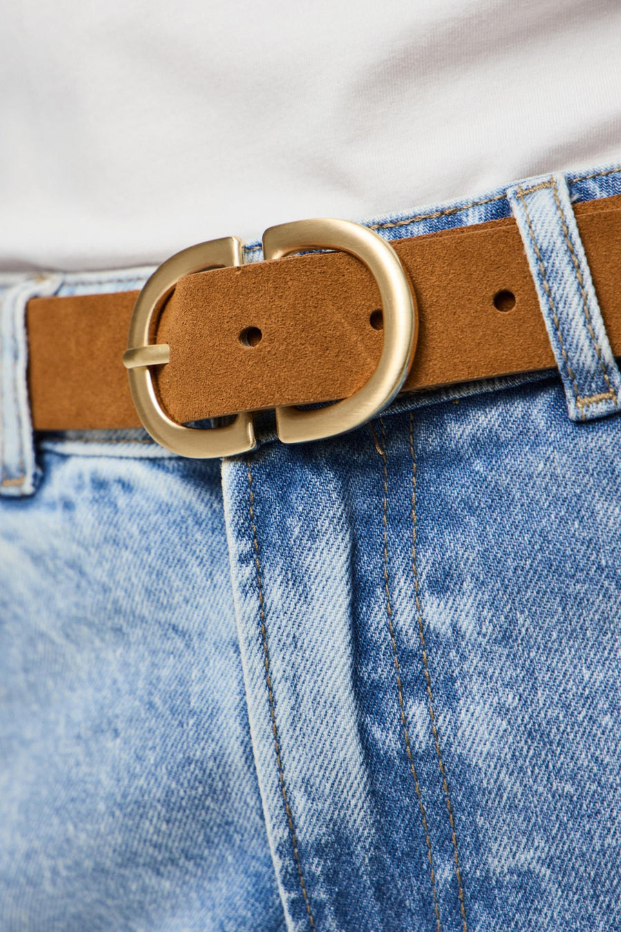 Bruine riem van PIECES, met een ronde gouden gesp en gedragen op een blauwe spijkerbroek.
