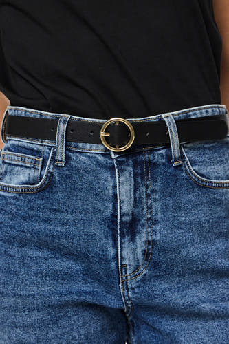 Ceinture noire PIECES® avec une boucle ronde dorée, portée avec des jeans bleus et un t-shirt noir.