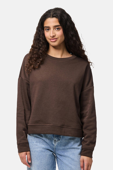 Bruine sweater van PIECES, gedragen met een blauwe jeans en gestyled met losse krullen.

