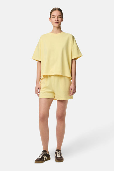 Gele short van PIECES®, gecombineerd met een bijpassend shirt en bruine sneakers.