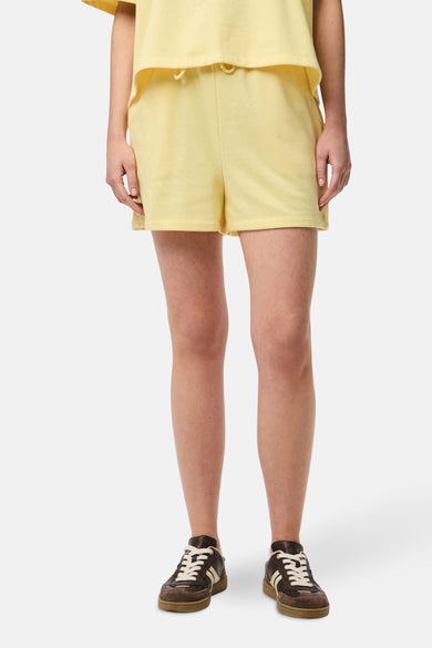 Gele short van PIECES, met een elastische tailleband en getoond met bruine lage schoenen.
