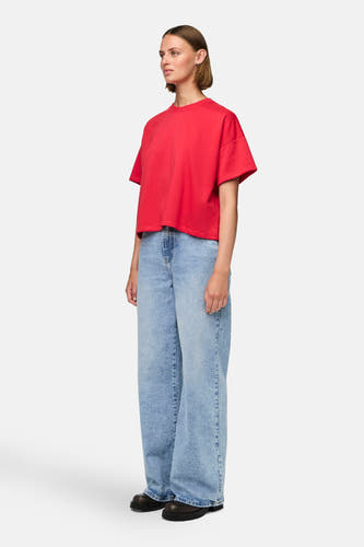 Rood T-shirt met korte mouwen van PIECES®, gedragen met wijde jeans en zwarte schoenen, staande.
