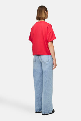 Rood T-shirt met korte mouwen van PIECES, gedragen met wijde, blauwe jeans, gezien van achteren.
