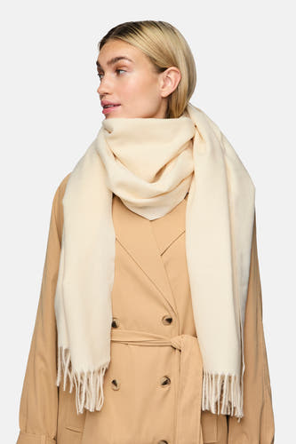 Beige wintersjaal van Pieces met franjes, gedragen met een bruine trenchcoat.
