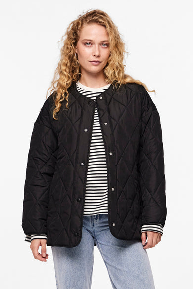 Zwarte korte jas van PIECES®, met een ruitvormig stiksel en gedragen over een gestreept shirt en jeans.
