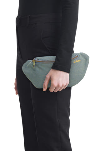 Sac à bandoulière bleu de PIECES avec fermeture éclair dorée, broderie 'be happy' et tissu texturé, porté par une personne vêtue de noir.