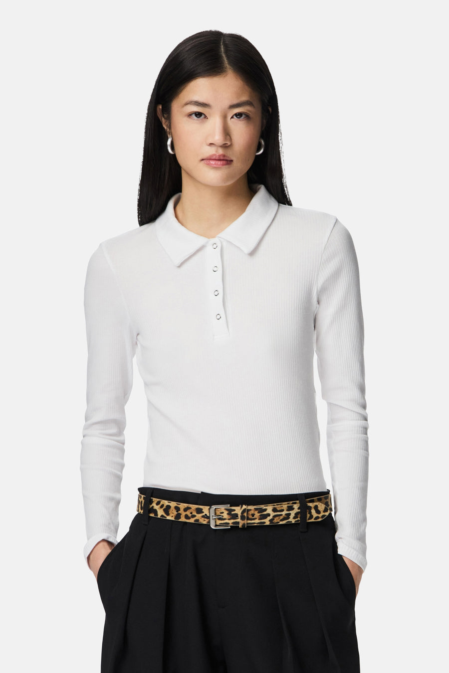 Vrouw met wit poloshirt met lange mouwen en zwarte broek met luipaardprint riem.