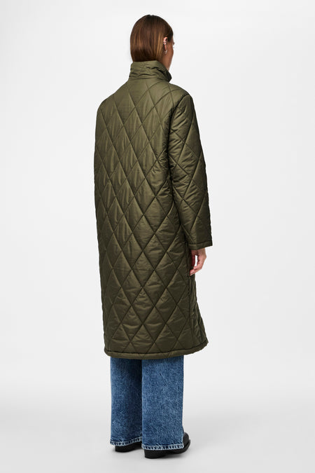 Groene lange jas van PIECES, met diamantstikselpatroon, gedragen met blauwe jeans en zwarte schoenen, gezien van achteren.
