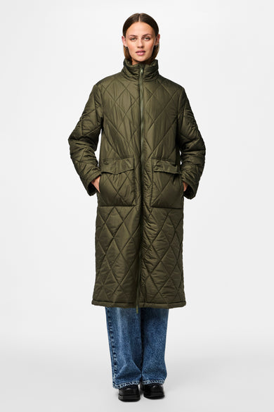Groene lange jas van PIECES® met doorgestikt ruitpatroon, zakken en gedragen met blauwe jeans en zwarte schoenen.
