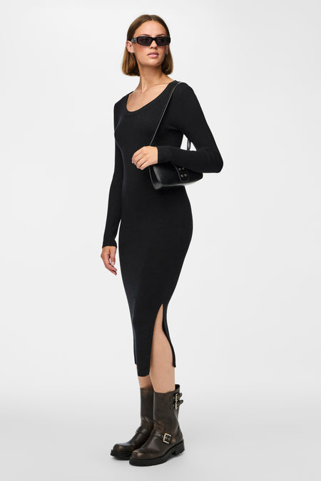Zwarte jurk met lange mouwen van PIECES®, met split en gedragen met bruine laarzen en een zwarte handtas.
