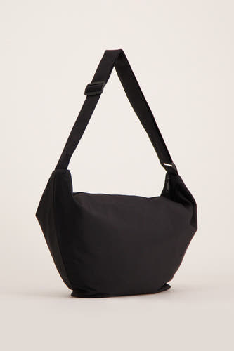 Sac à dos noir de PIECES®, avec une sangle d'épaule ajustable et une fermeture éclair, posé sur un fond crème.