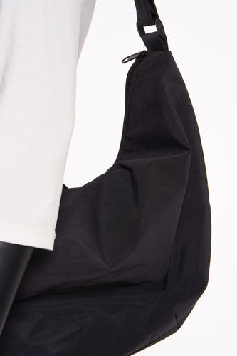 Sac à dos noir de PIECES®, avec une fermeture éclair et une bandoulière ajustable, porté sur un t-shirt blanc.