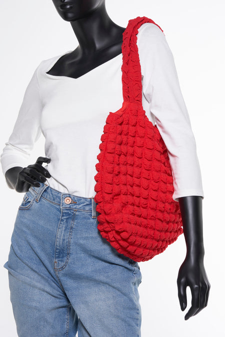 Sac à main rouge de PIECES®, avec texture en relief, porté par un mannequin vêtu d'une chemise blanche et d'un short en jean.