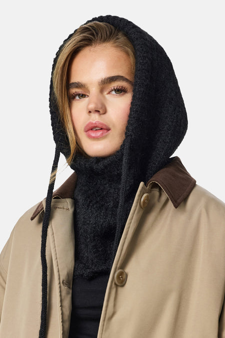 Zwarte hoed van PIECES®, met dikke gebreide textuur en koorden, gecombineerd met beige jas met bruine kraag.
