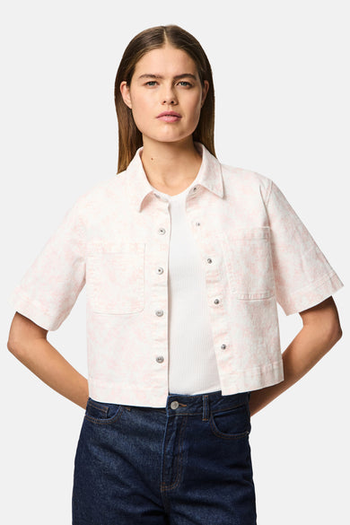 Chemise rose à manches courtes de PIECES®, avec un imprimé floral, portée sur une chemise blanche et un jeans bleu marine.