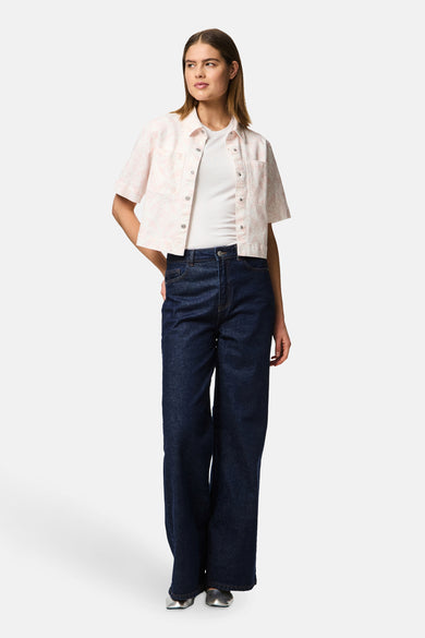 Roze hemd met korte mouwen van PIECES®, met bloemenpatroon, gedragen over een wit shirt en een donkerblauwe jeans.
