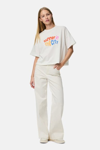 T-shirt blanc à manches courtes de PIECES®, avec une impression de texte 'Summer in the City' colorée, associé à des jeans blancs et des baskets.