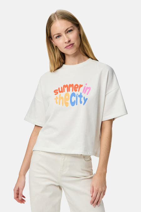 Wit T-shirt met korte mouwen van PIECES®, met kleurrijke "summer in the City" tekstprint, gedragen met een witte broek.

