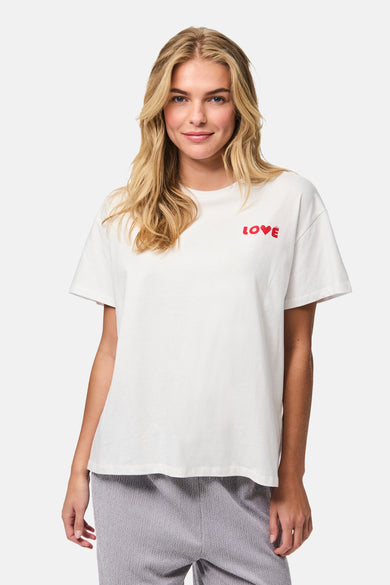 Wit T-shirt met korte mouwen van PIECES®, met rode "LOVE" tekst erop, gedragen met een grijze broek.
