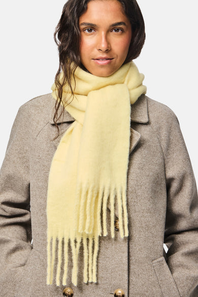 Gele wintersjaal van PIECES®, met gerafelde uiteinden, gecombineerd met een bruine jas.
