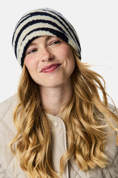 Meerkleurige muts van PIECES® met blauwe en witte strepen, gedragen door een vrouw met een beige jas.
