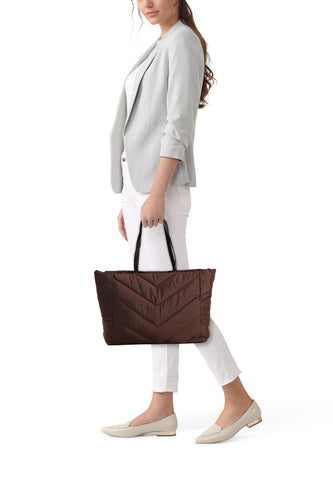 Vrouw met grijze blazer, witte broek en bruine shopper.