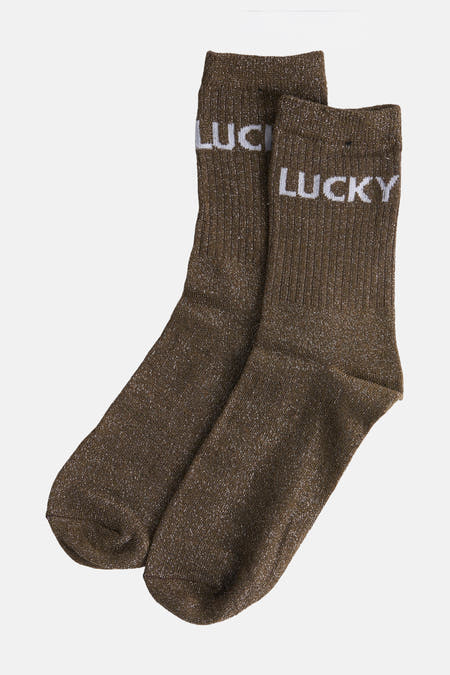 Kaki sokken van PIECES®, met een glinsterende textuur en het woord "LUCKY" in witte letters.
