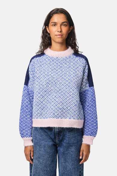 Multikleurige trui met ronde hals van PIECES, met ruitpatroon en roze ribgebreide boorden, gedragen met een blauwe jeans.
